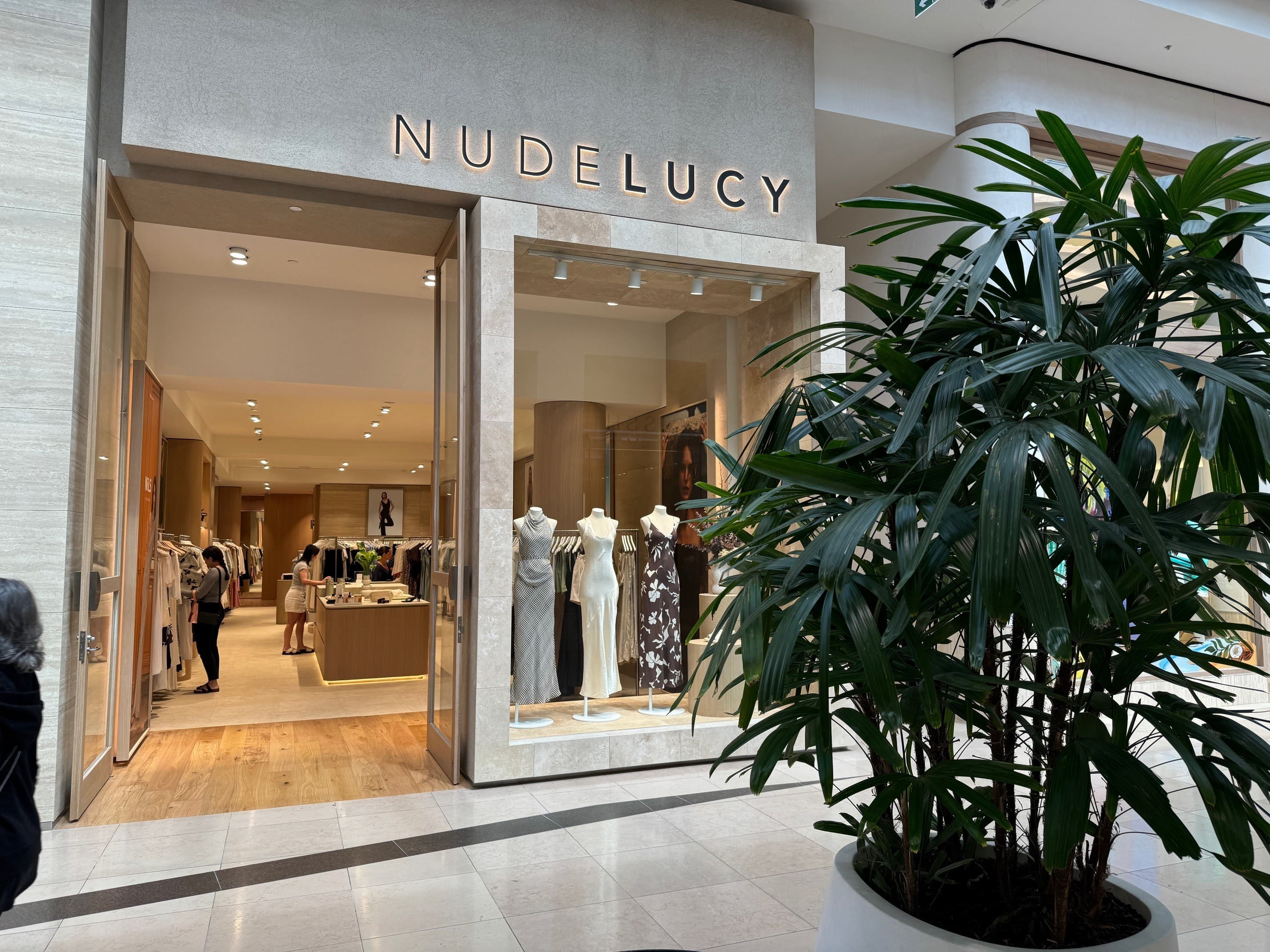 Nude Lucy store with mannequins in the window and an indoor plant in the foreground
