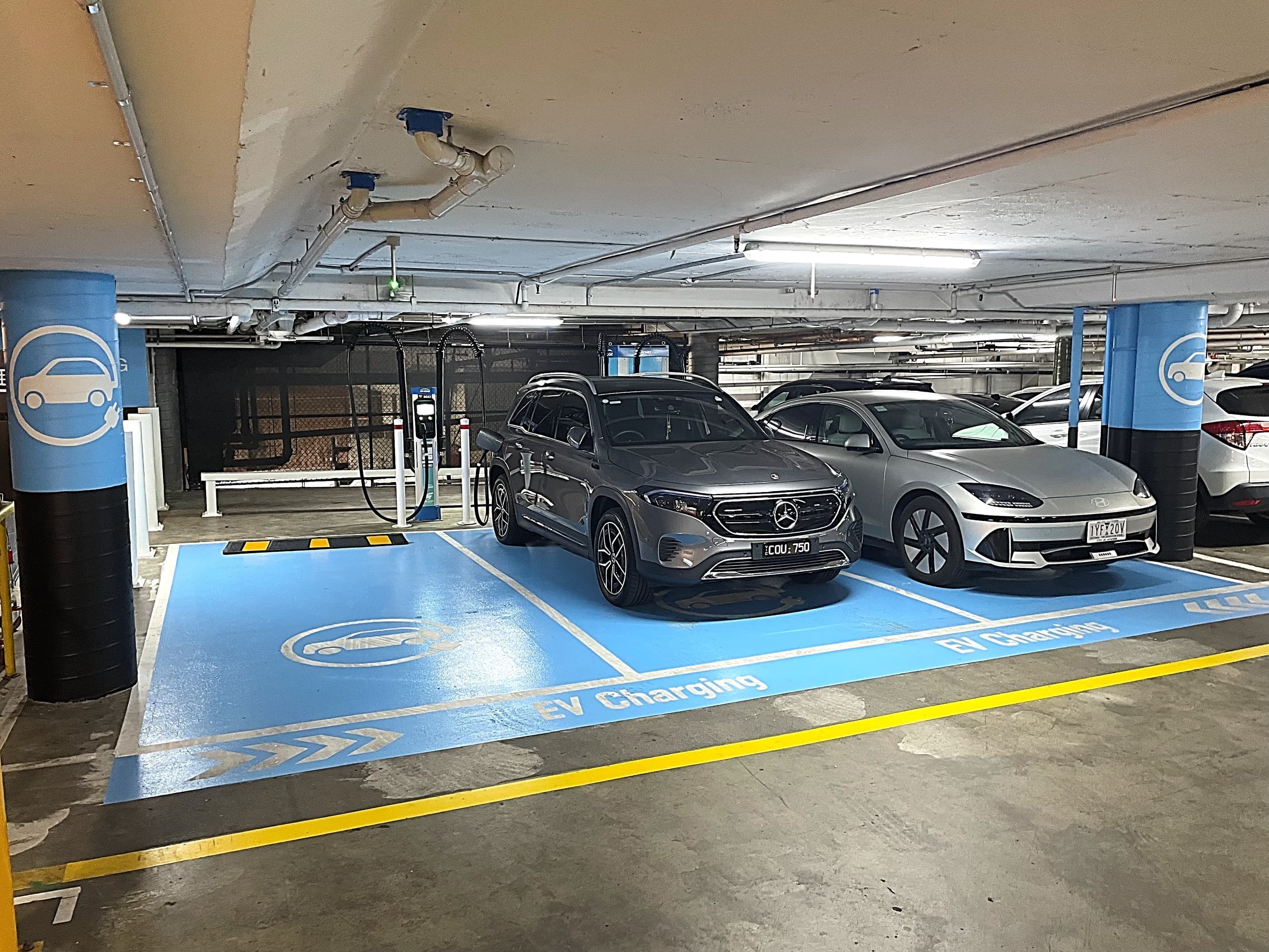two silver cars in blue EV charging bays in an underground car park
