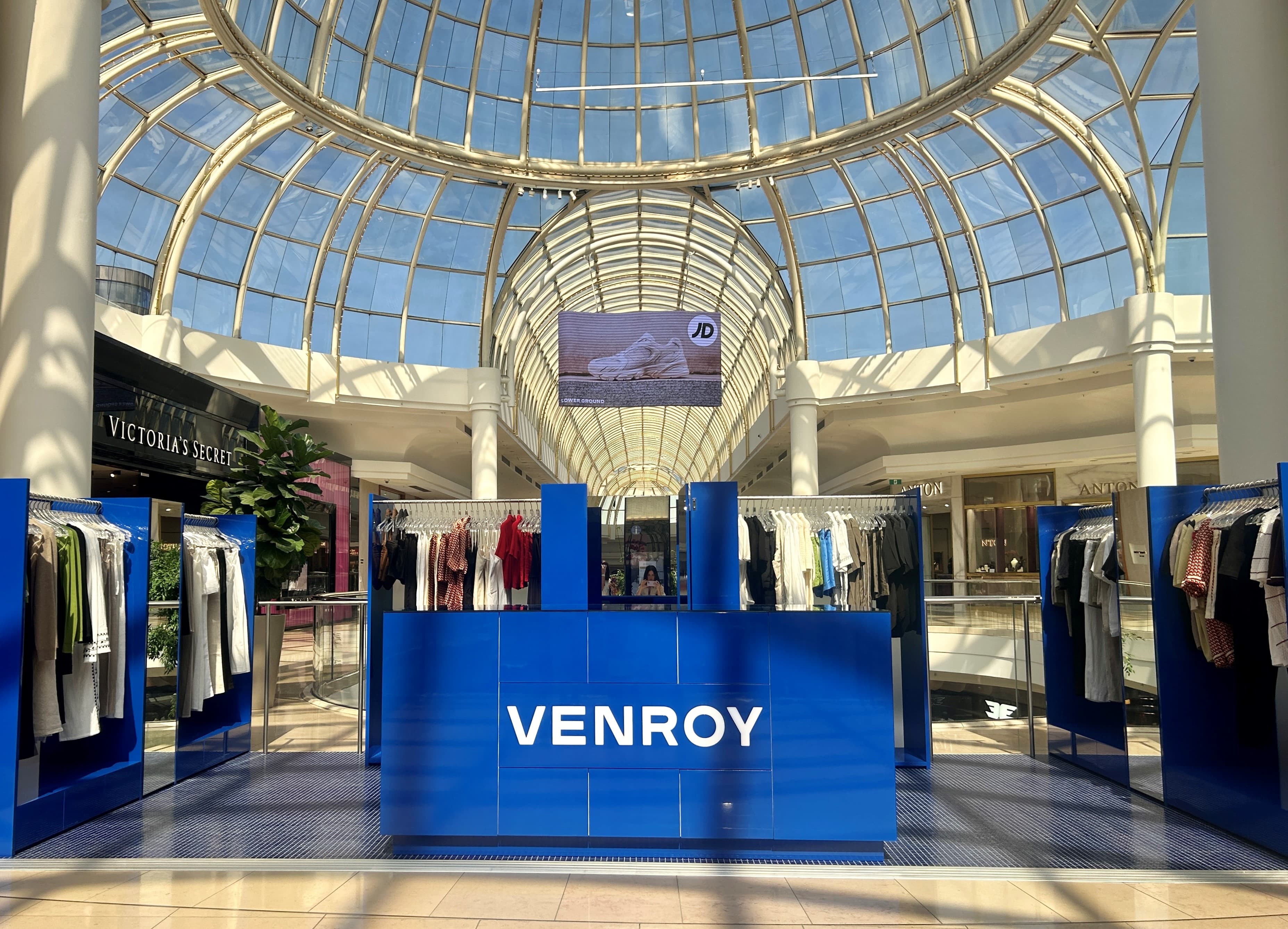 A Venroy pop up kiosk with blue clothing stands under a gridshell roof