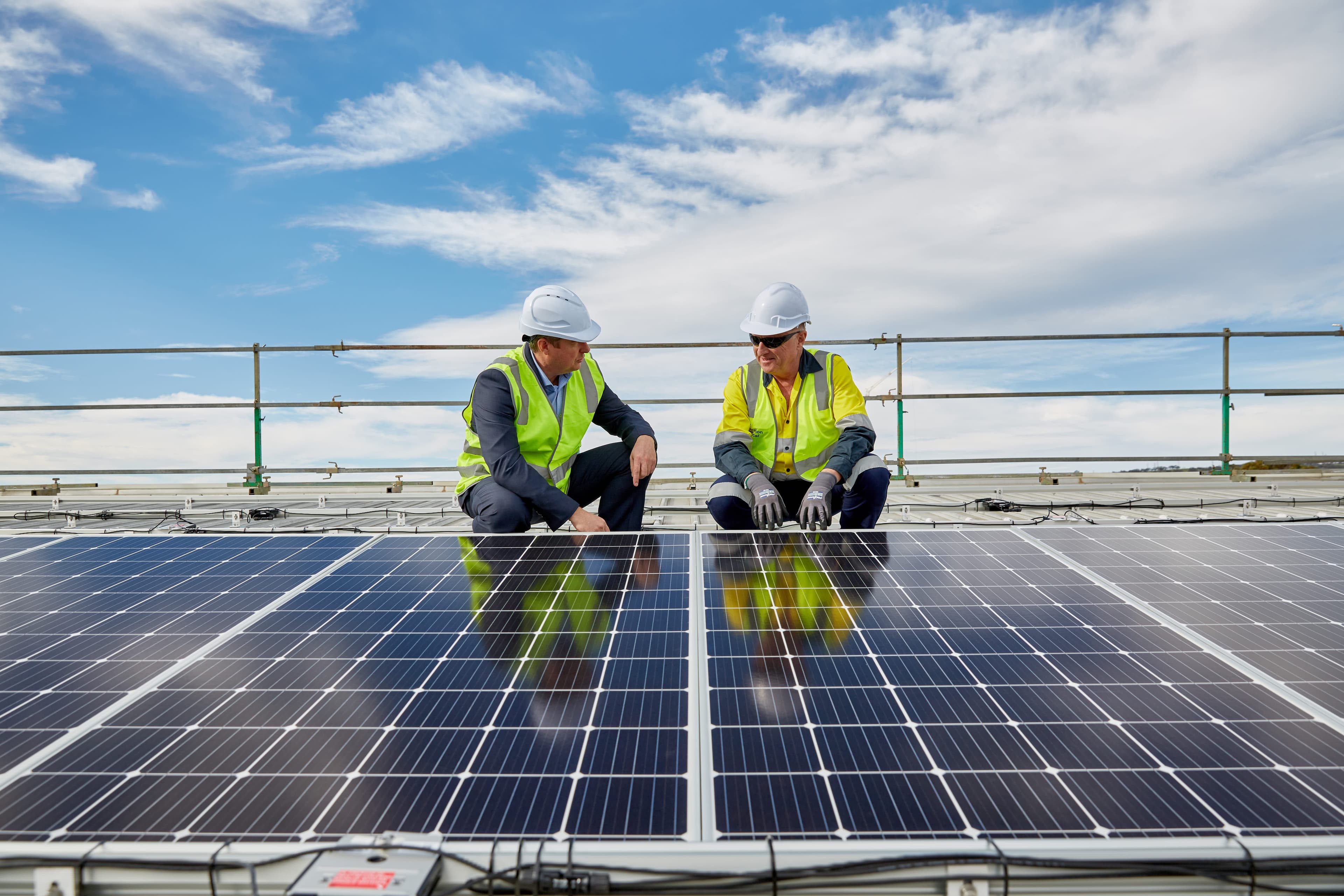 Two people in yellow hi-vis jackets crouched over rooftop solar panels