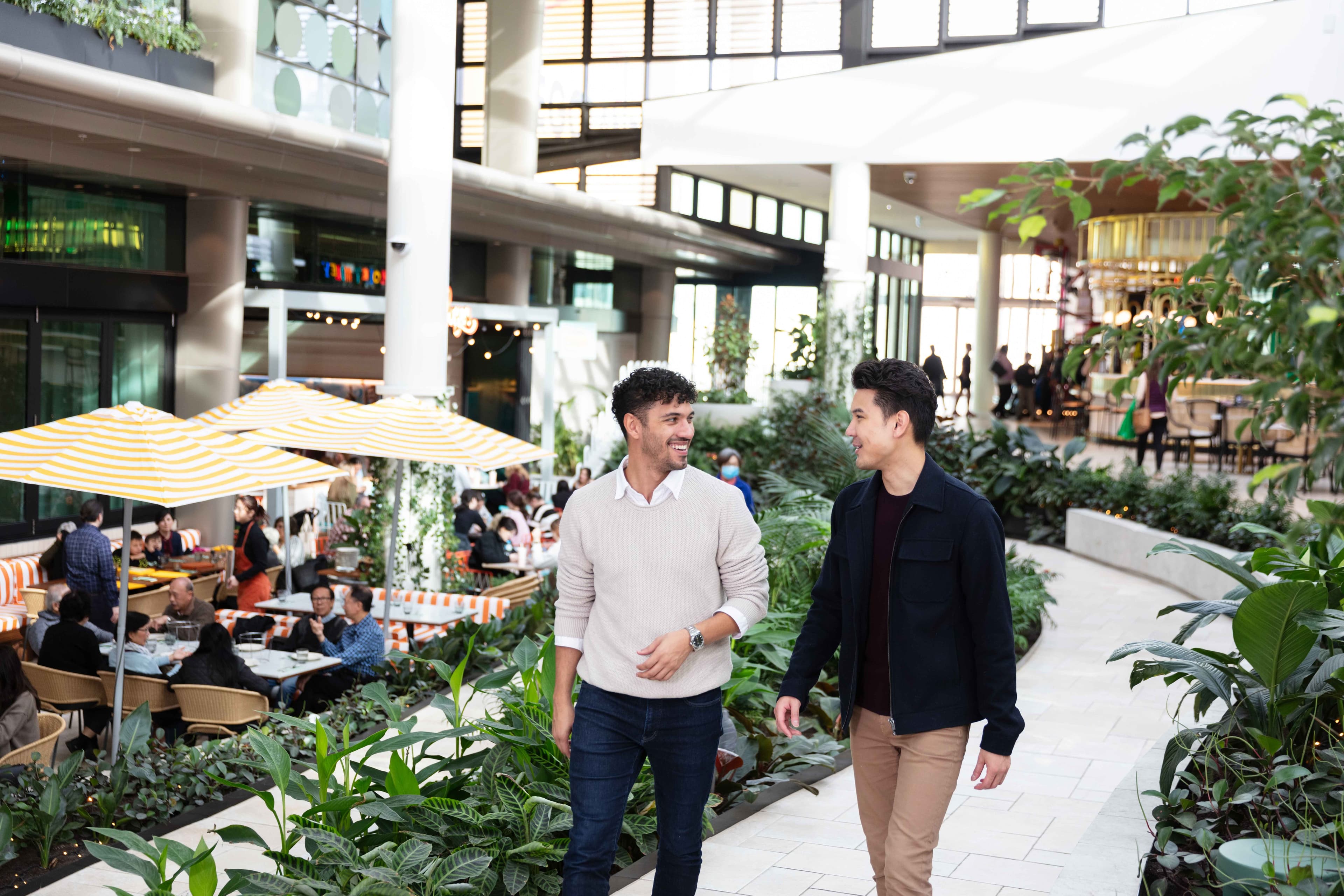 Two people walking and talking through an indoor garden with parasols